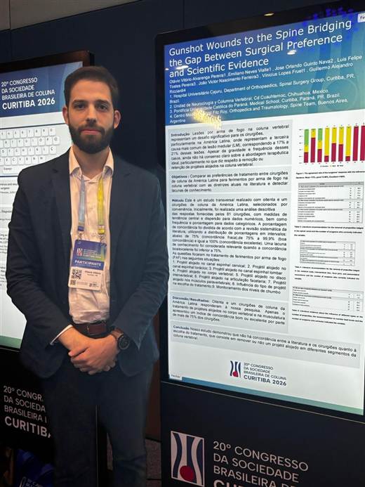 Dr. Otávio Vitório ao lado de pôster científico sobre ferimentos por arma de fogo na coluna, no 20º Congresso da Sociedade Brasileira de Coluna